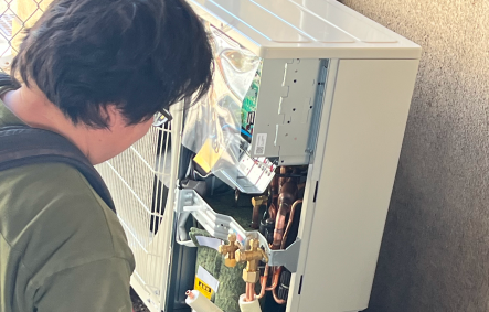 室外機の配電盤を開けて入れ替え工事を行っている作業員